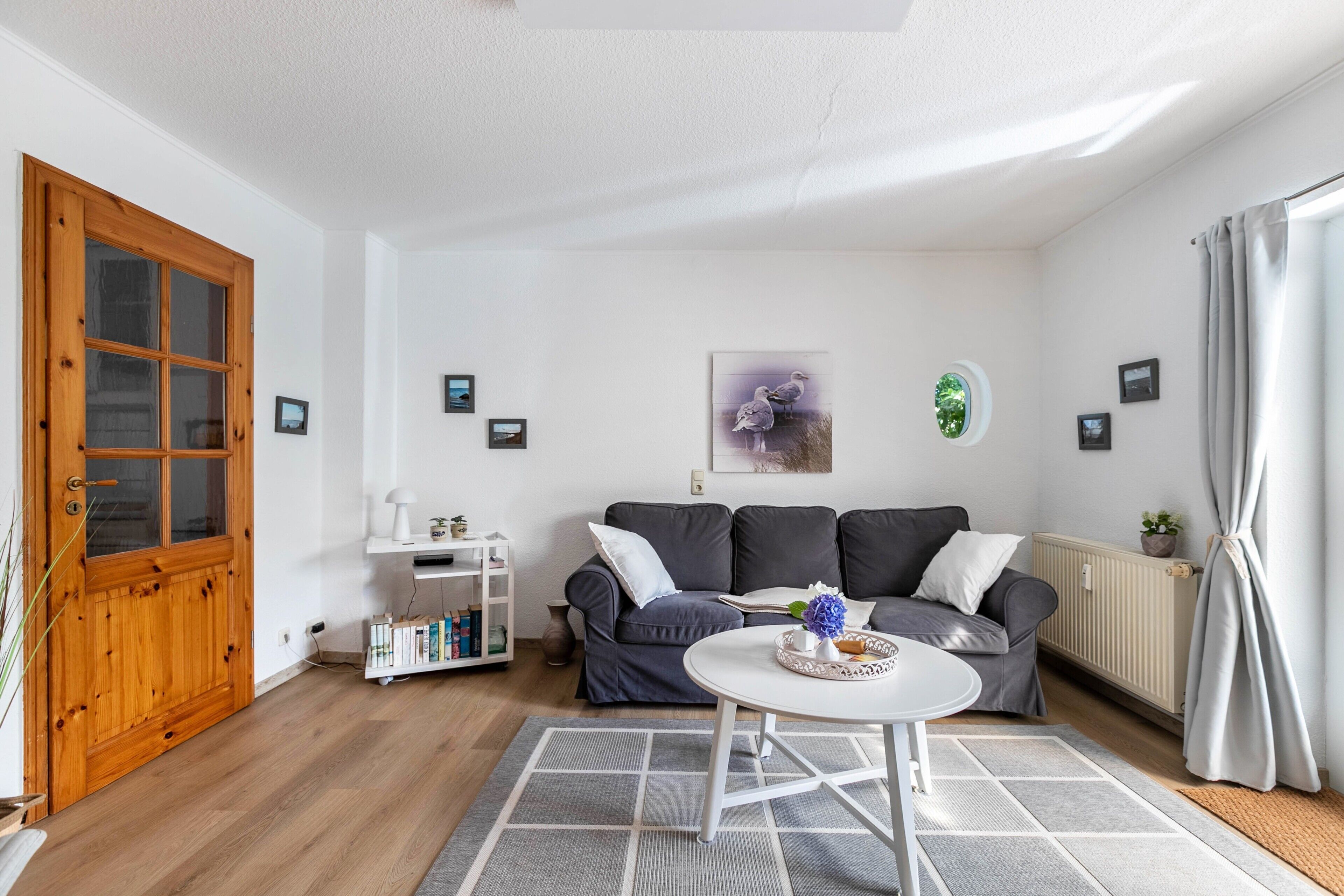 A living room with a wooden door, a grey sofa, a white coffee table, and a grey rug.