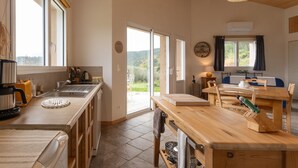 A kitchen with a large window, a wooden table, and a view of the outdoors. - Holiday Home 'Eco Gîte' with Mountain View, Wi-Fi and Air Conditioning (Payzac)