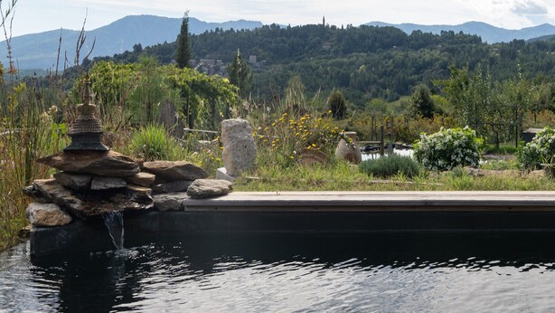 A serene outdoor area with a stone water feature, lush greenery, and a distant mountain range. - Holiday Home 'Eco Gîte' with Mountain View, Wi-Fi and Air Conditioning (Payzac)