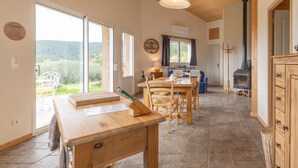 A spacious kitchen with a large window, a dining area with wooden furniture, and a stone floor. - Holiday Home 'Eco Gîte' with Mountain View, Wi-Fi and Air Conditioning (Payzac)