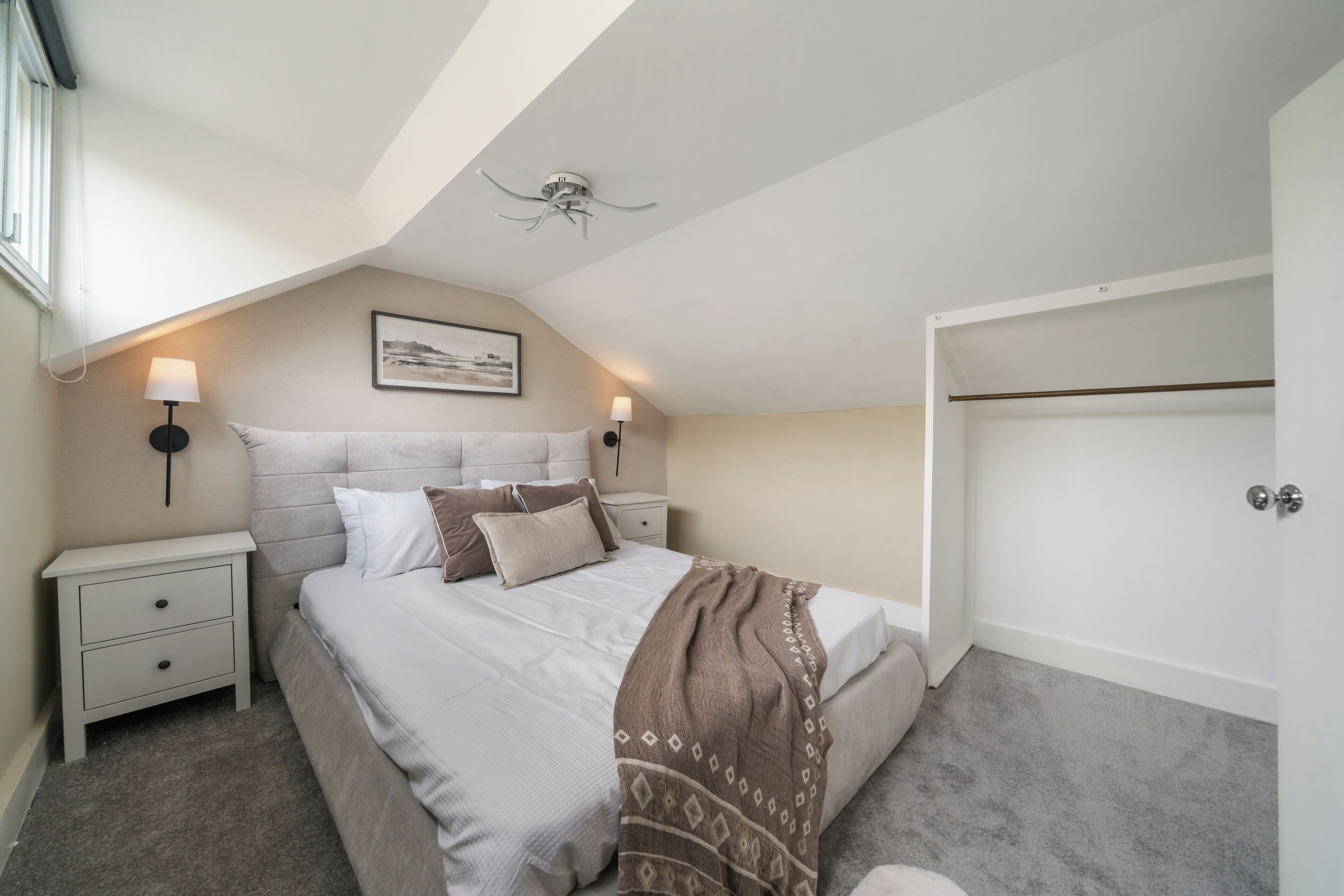 Une chambre à coucher comprenant un lit, des tables de chevet, un ventilateur de plafond, une lampe fixée au mur et une armoire.