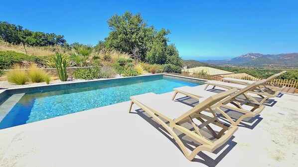 Una piscina con agua cristalina, rodeada de sillas de descanso y vistas a montañas.