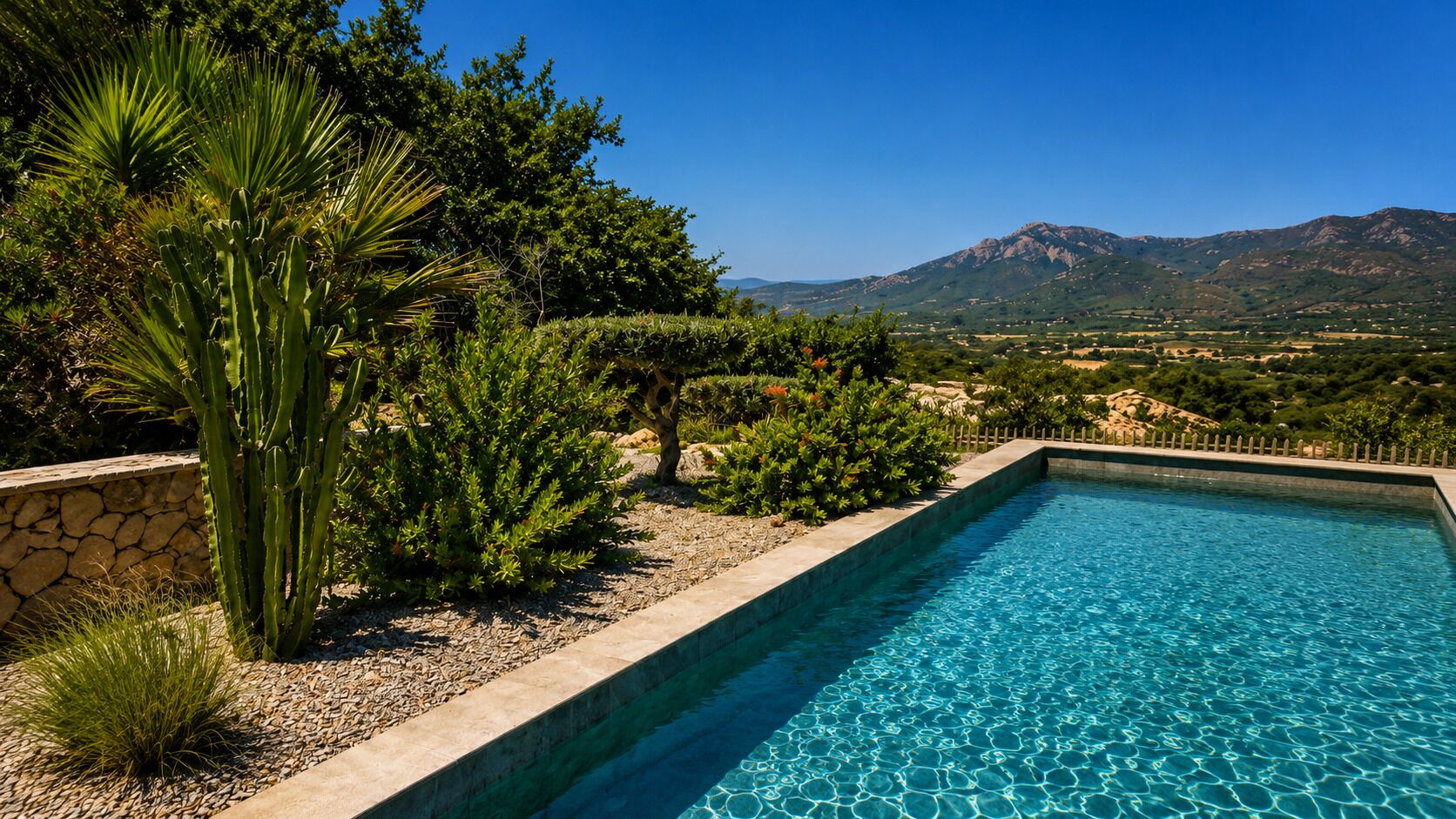 A rectangular swimming pool with clear blue water, surrounded by a stone wall and various green plants.