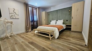 Una camera da letto con un letto, una panca, un armadio, un comodino e una lampada a parete.