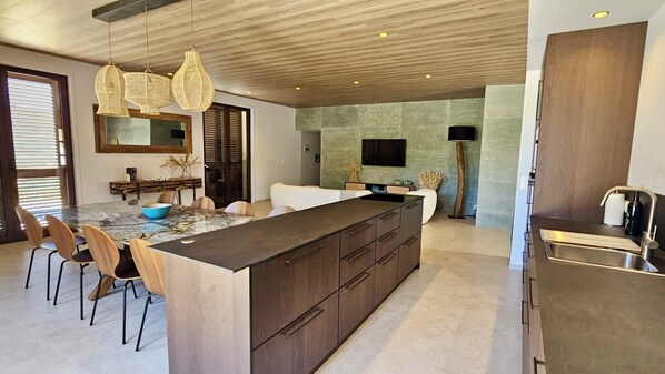 A modern kitchen with a large island, wooden cabinets, and a dining area with chairs. - VILLA MODERNE EN CORSE - Sea and mountain views, swimming pool, pool house (CALENZANA)