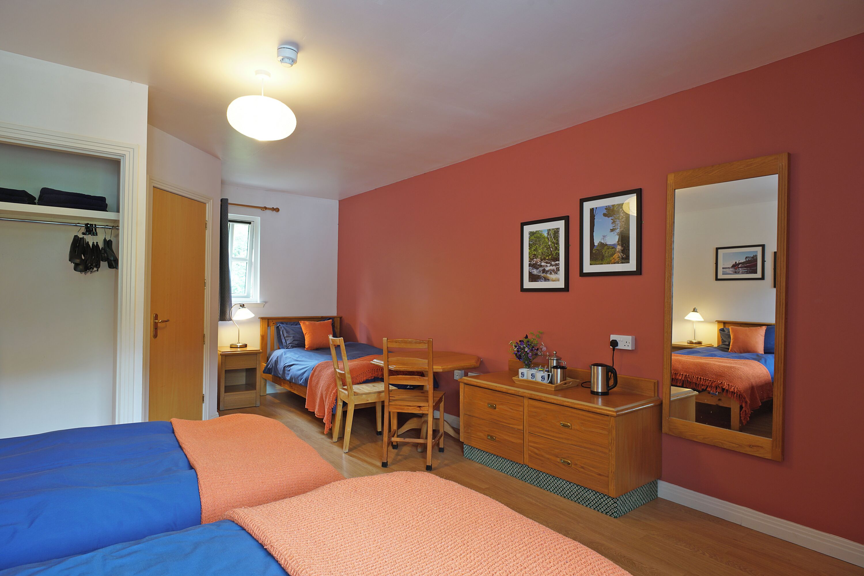 A bedroom with two beds, a wooden dresser, a desk, and a mirror.