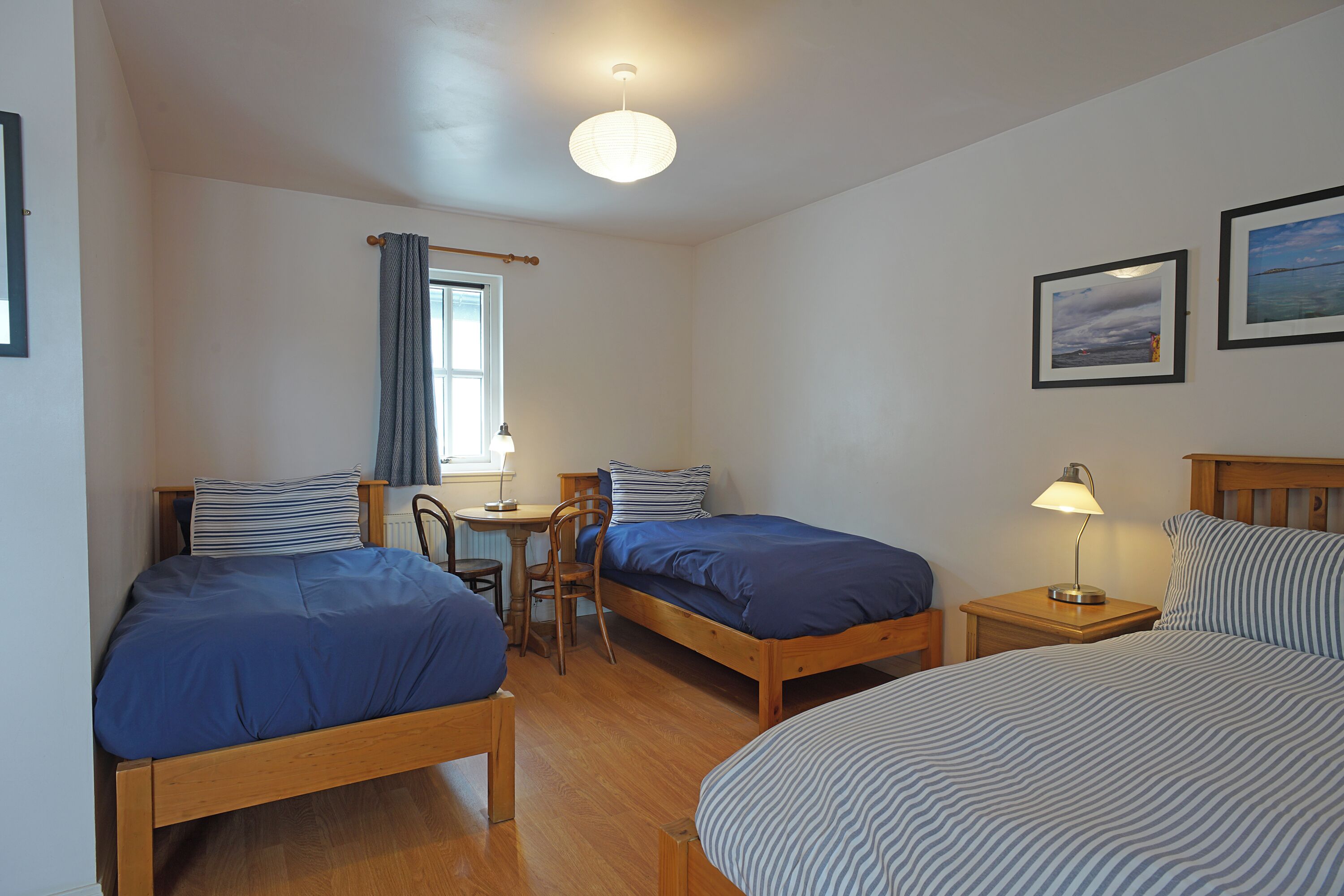 A room with two single beds, a wooden desk, a chair, a table, and a lamp.
