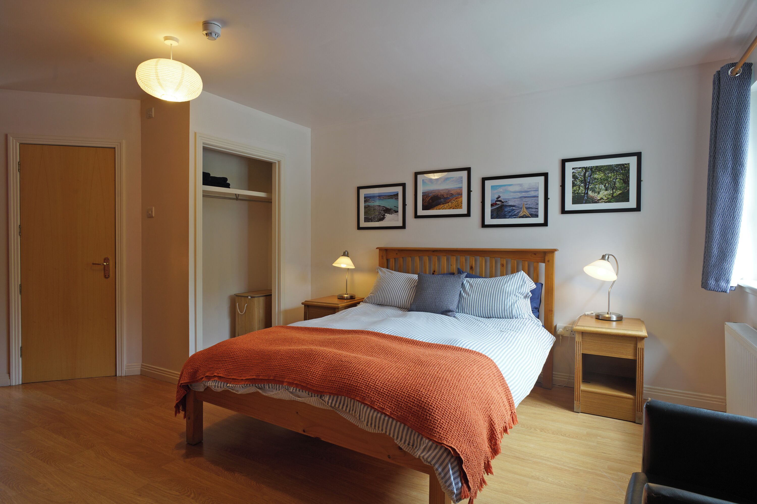 Une chambre à coucher avec un lit en bois, deux tables de chevet avec des lampes, une armoire et trois tableaux encadrés accrochés au mur.