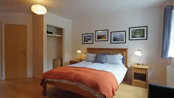 Un dormitorio con una cama de madera, dos mesitas de noche con lámparas, un armario y tres cuadros enmarcados en la pared.