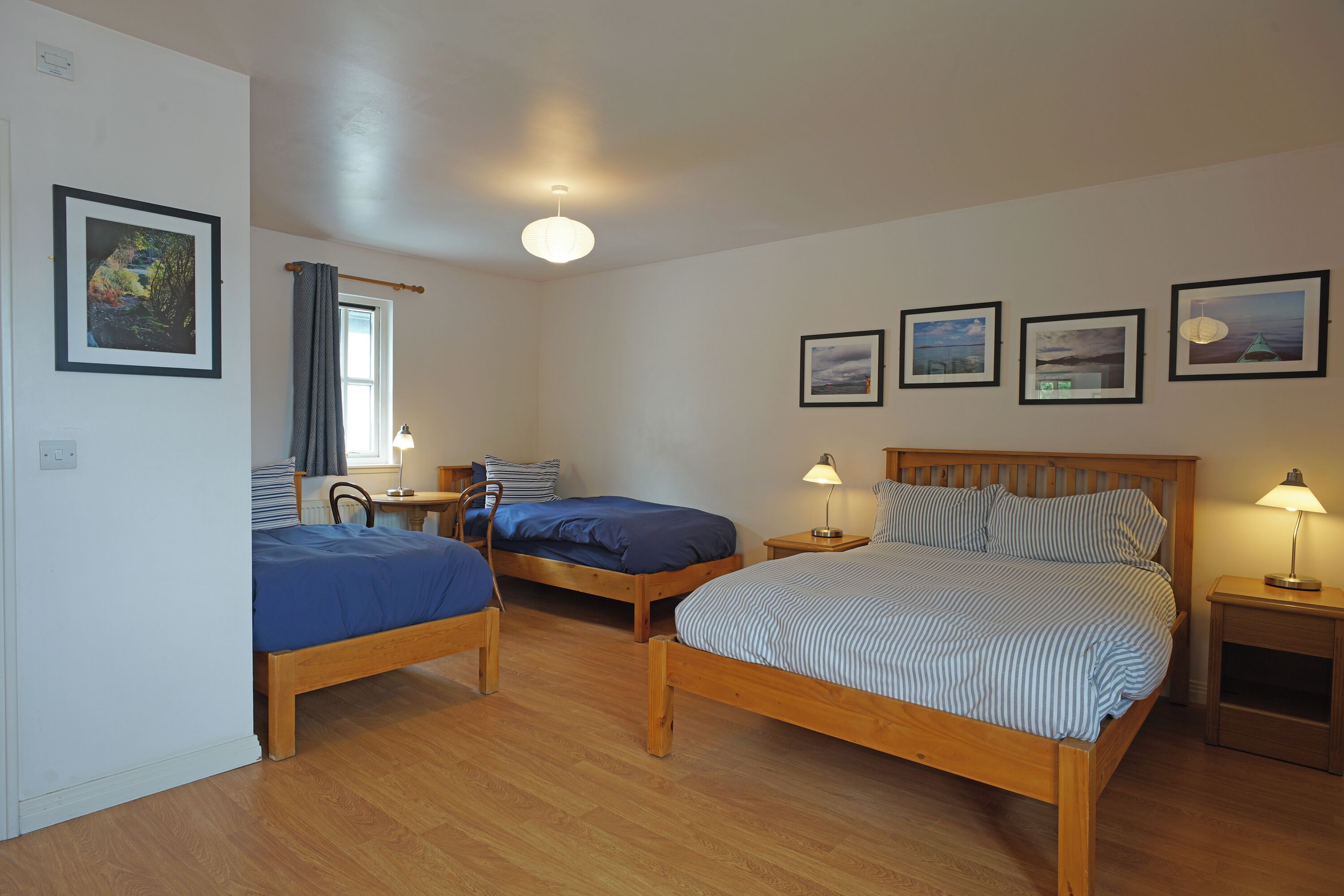 A room with three wooden beds, a window with curtains, and framed pictures on the wall.