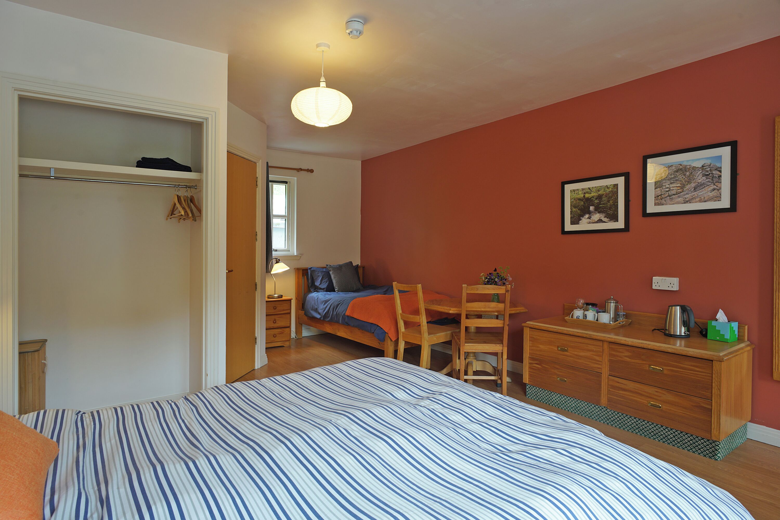 A bedroom with a bed, a wooden dresser, a chair, a desk, and a closet.