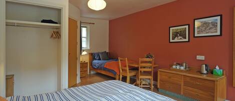 A bedroom with a bed, a wooden dresser, a chair, a desk, and a closet.