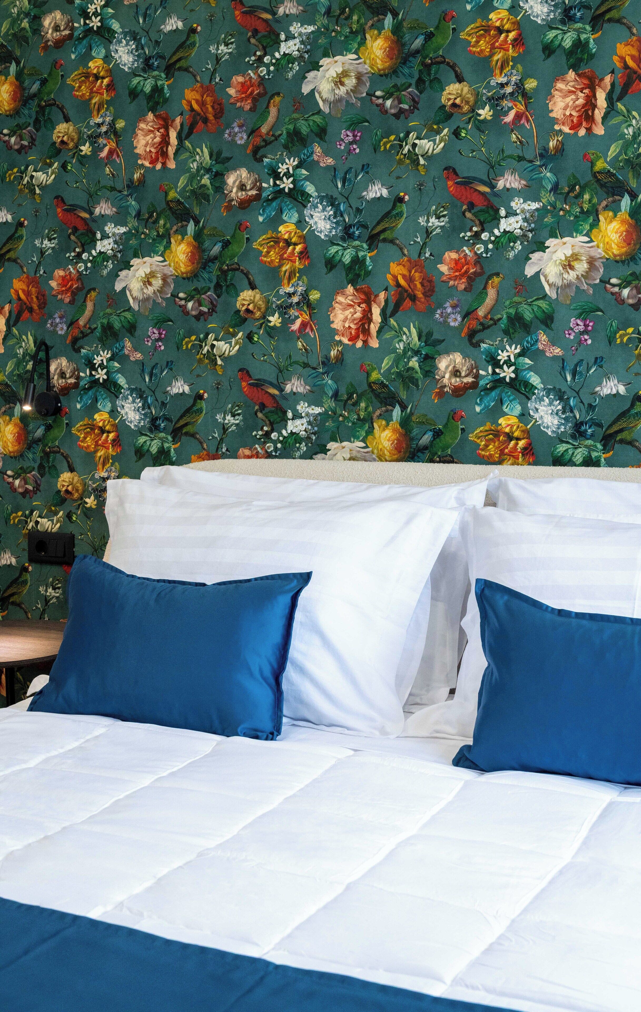 A bed with white and blue bedding, a floral wallpaper background, and a wooden headboard.
