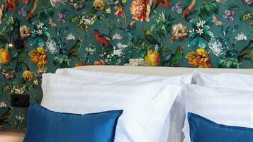 A bed with white and blue bedding, a floral wallpaper background, and a wooden headboard.