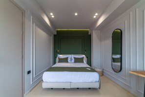 A modern bedroom with a large bed, a green accent wall, a mirror, and recessed ceiling lights. - 4 Living by Semavi (Heraklion)