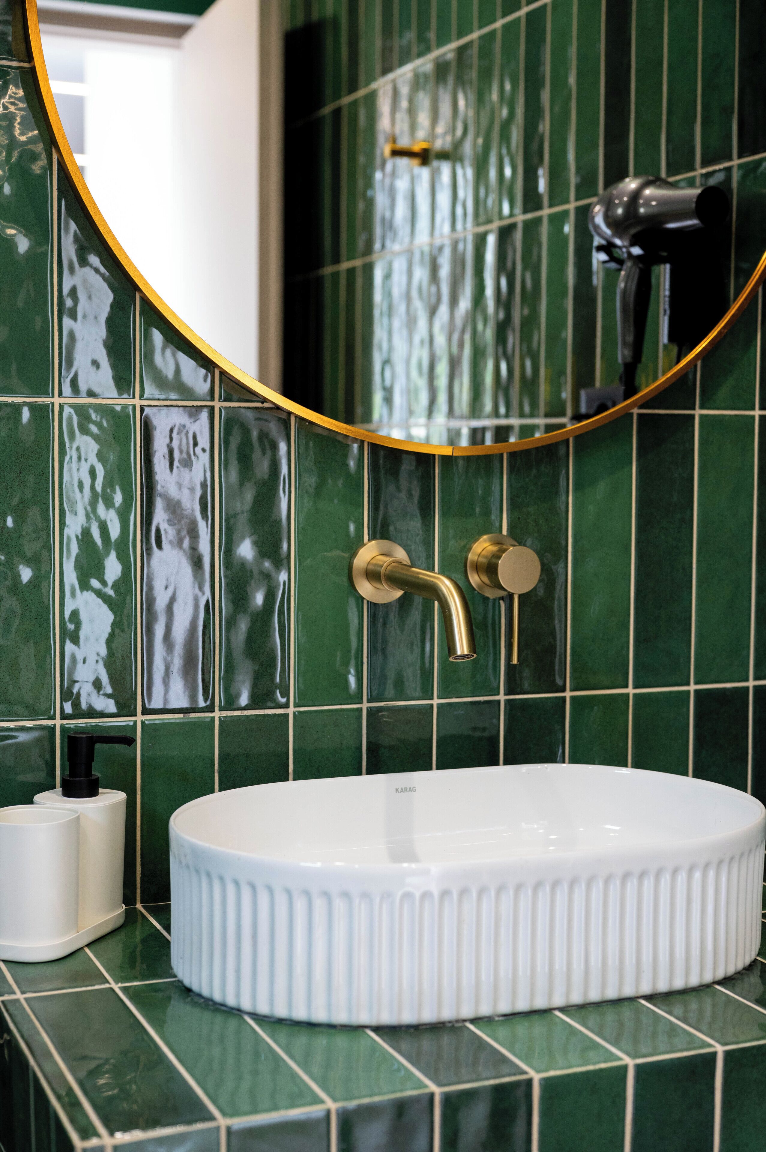 Un baño con un lavamanos blanco, paredes con azulejos verdes y un espejo con marco dorado.