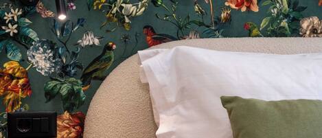 A bedroom with a floral wallpaper, a round black side table, and a bed with white and green pillows.