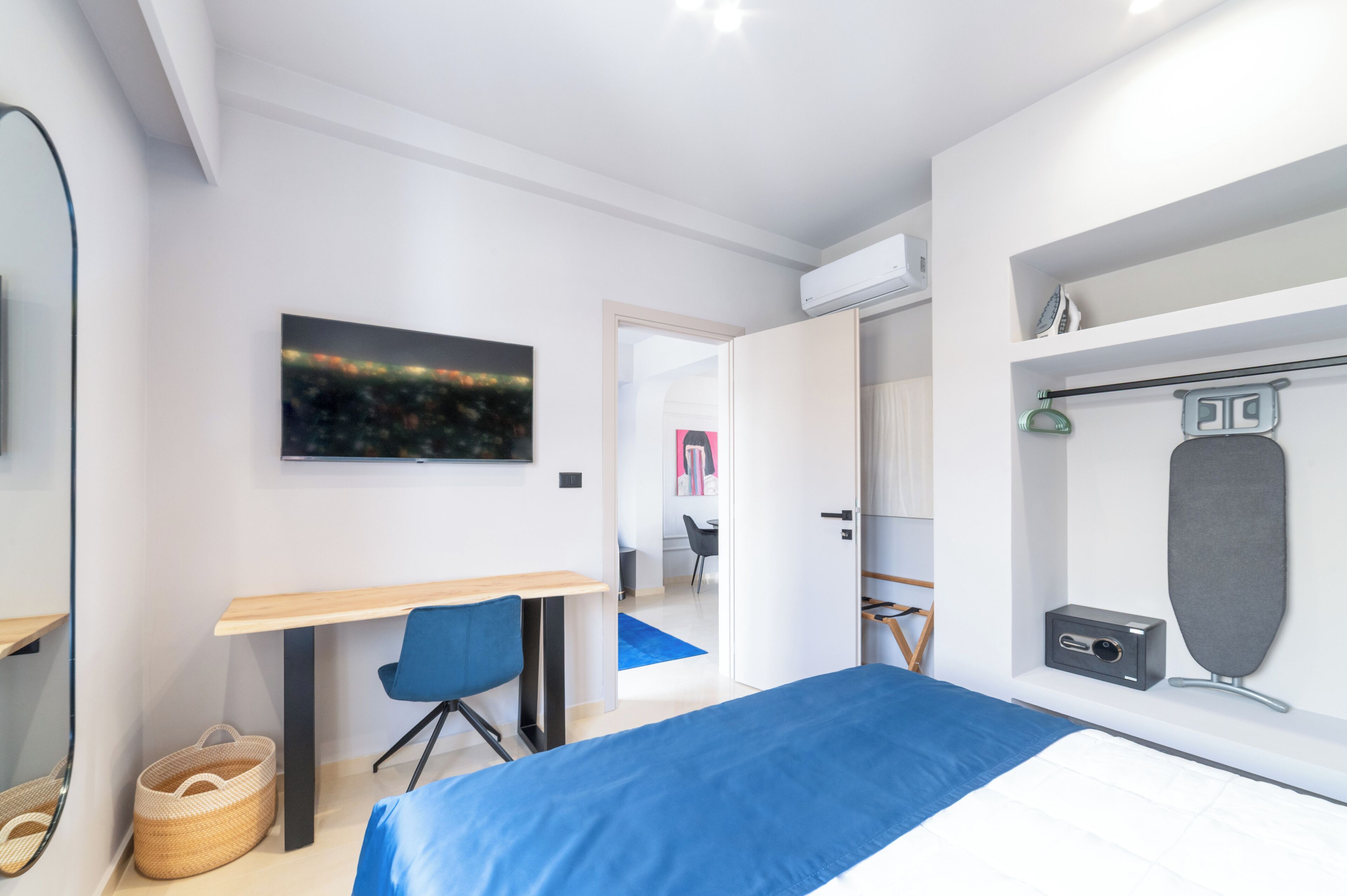 Une chambre d’hôtel moderne équipée d’un lit, d’un bureau, d’une chaise, d’une armoire et ornée d’un tableau représentant un paysage urbain.