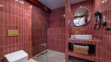 Un baño moderno con baldosas rojas, cabina de ducha con paredes de vidrio, lavabo blanco y secador de pelo fijado en la pared.