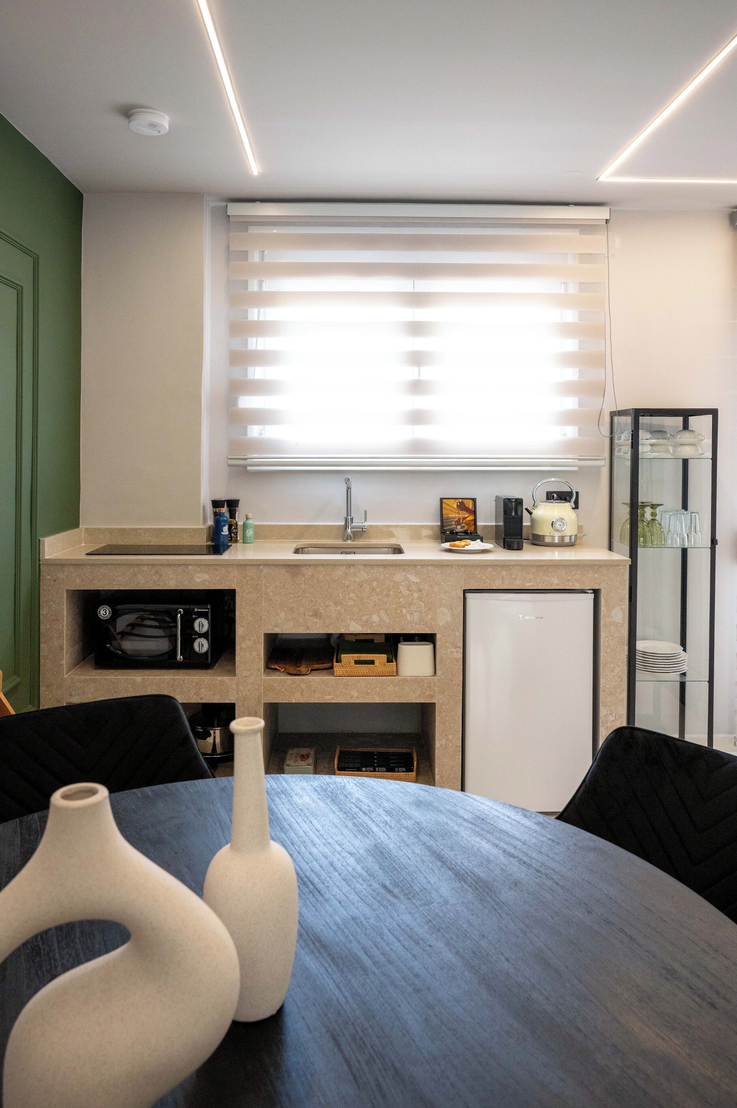 A modern kitchen with a built-in microwave, oven, and refrigerator. There is a window with blinds, a sink, and a countertop with various items.