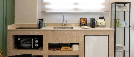 A modern kitchen with a built-in microwave, oven, and refrigerator. There is a window with blinds, a sink, and a countertop with various items.