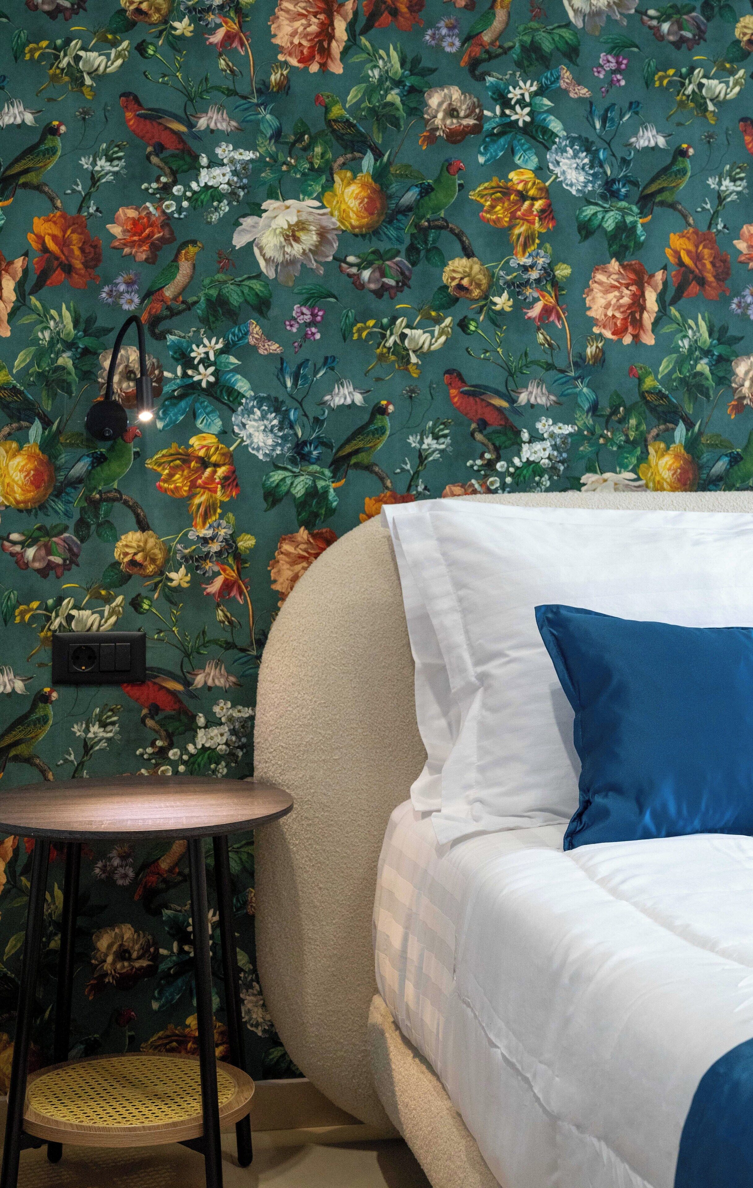 Ein Schlafzimmer mit floraler Tapete, einem runden Holztisch und einem Bett mit weißer und blauer Bettwäsche.