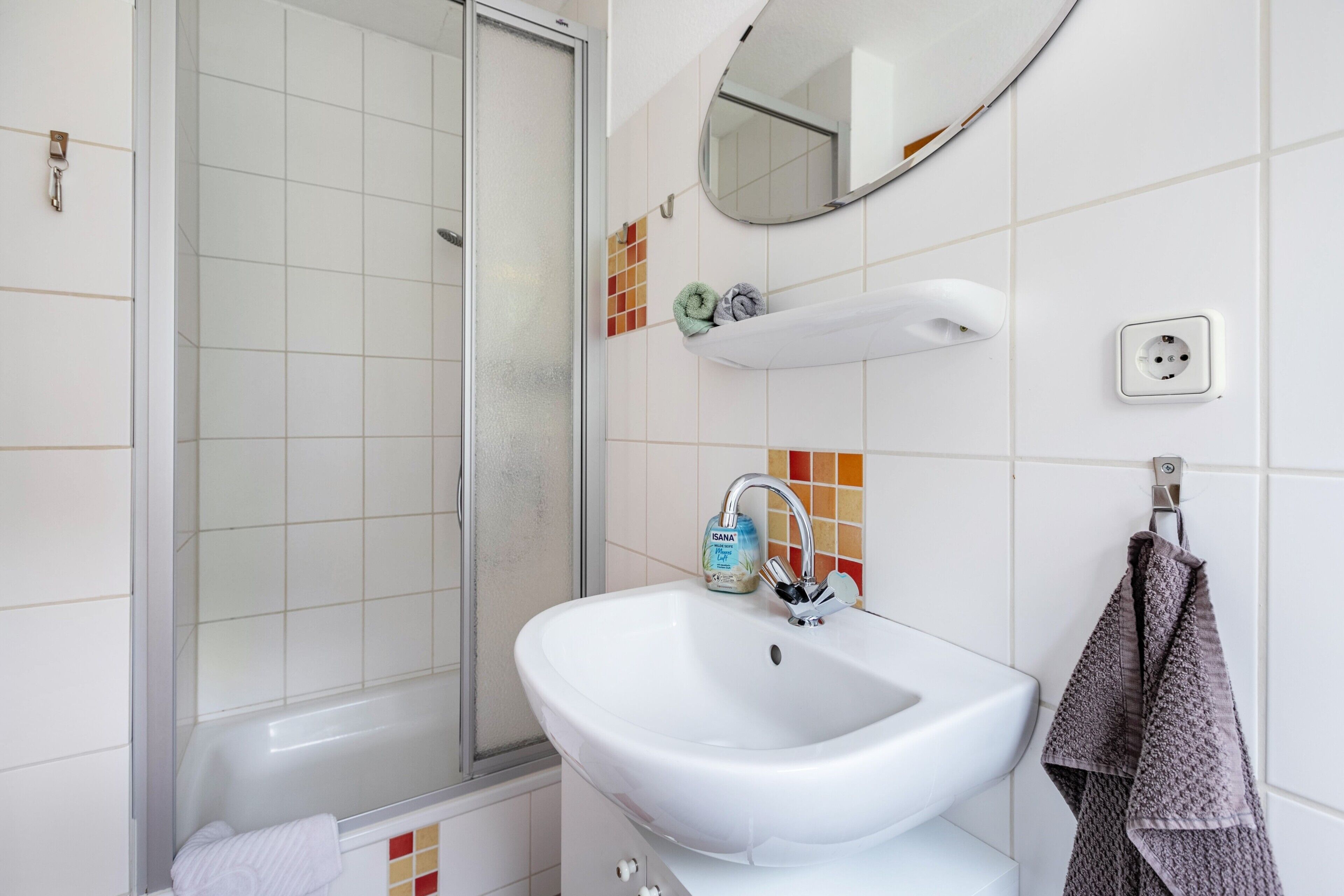 Une salle de bain avec un lavabo blanc, un miroir, un porte-serviettes et une douche.