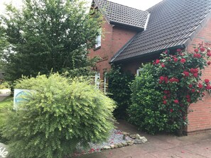 A brick building with a tiled roof, surrounded by lush greenery and red flowers. - Apartment 'Dohle No 1' with Shared Terrace, Shared Garden and Wi-Fi (Vollerwiek)