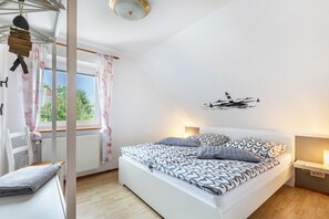 A bedroom with a bed, a chair, a window with curtains, a wall-mounted light, and a radiator. - Apartment 'Dohle No 1' with Shared Terrace, Shared Garden and Wi-Fi (Vollerwiek)