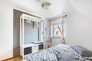 Une chambre à coucher comprenant un lit, une armoire intégrée, une fenêtre avec des rideaux et un radiateur.