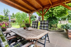 An outdoor patio with a wooden table and chairs, surrounded by greenery and potted plants. - Apartment 'Dohle No 1' with Shared Terrace, Shared Garden and Wi-Fi (Vollerwiek)