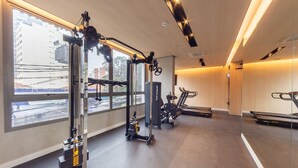 Et fitnesscenter med træningsudstyr, store vinduer og udsigt over byen.