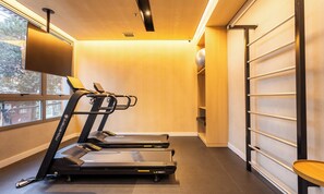 A small, modern gym with two treadmills, a wall-mounted TV, and a wooden shelf. - Modern Apartments With Fitness Area and Coworking in the Best Location of Pompeia, SP - DIO (São Paulo)
