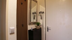 Un baño con puerta de madera, un espejo, un lavamanos, una planta en maceta y una lámpara de pared.