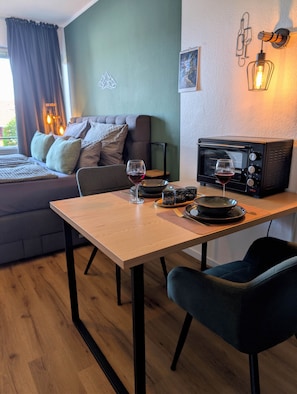 Ein Essbereich mit Tisch, Stühlen, einer Mikrowelle, Weingläsern und einer Couch.