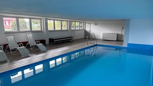Una piscina interior con agua azul cristalina, sillones blancos para relajarse y una escalera.