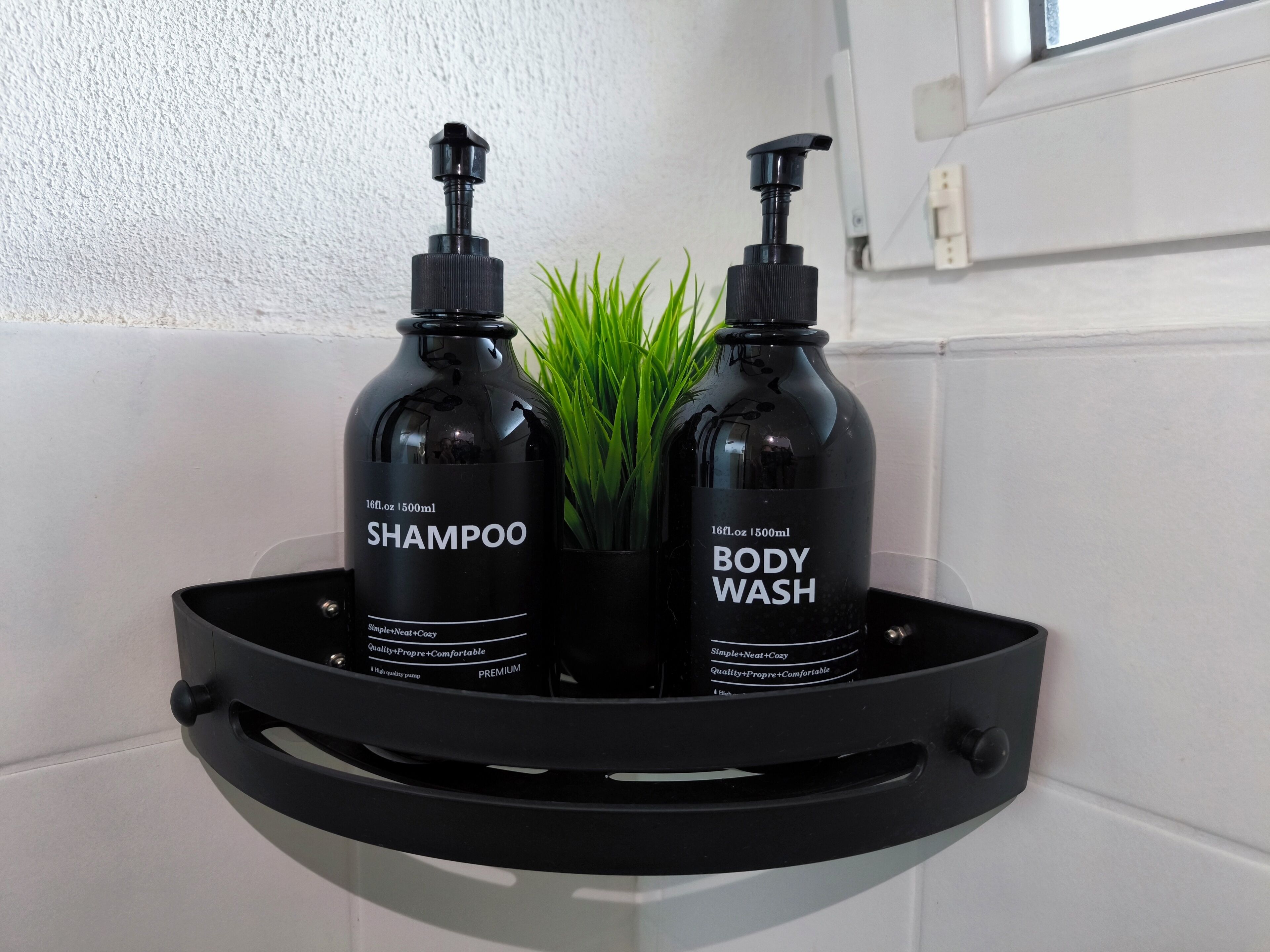 Twee zwarte flessen shampoo en douchegel op een zwarte dienblad, met een plantje.