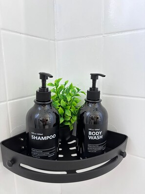 Un estante negro en el baño con dos botellas de champú y gel de baño, y una pequeña planta en maceta.