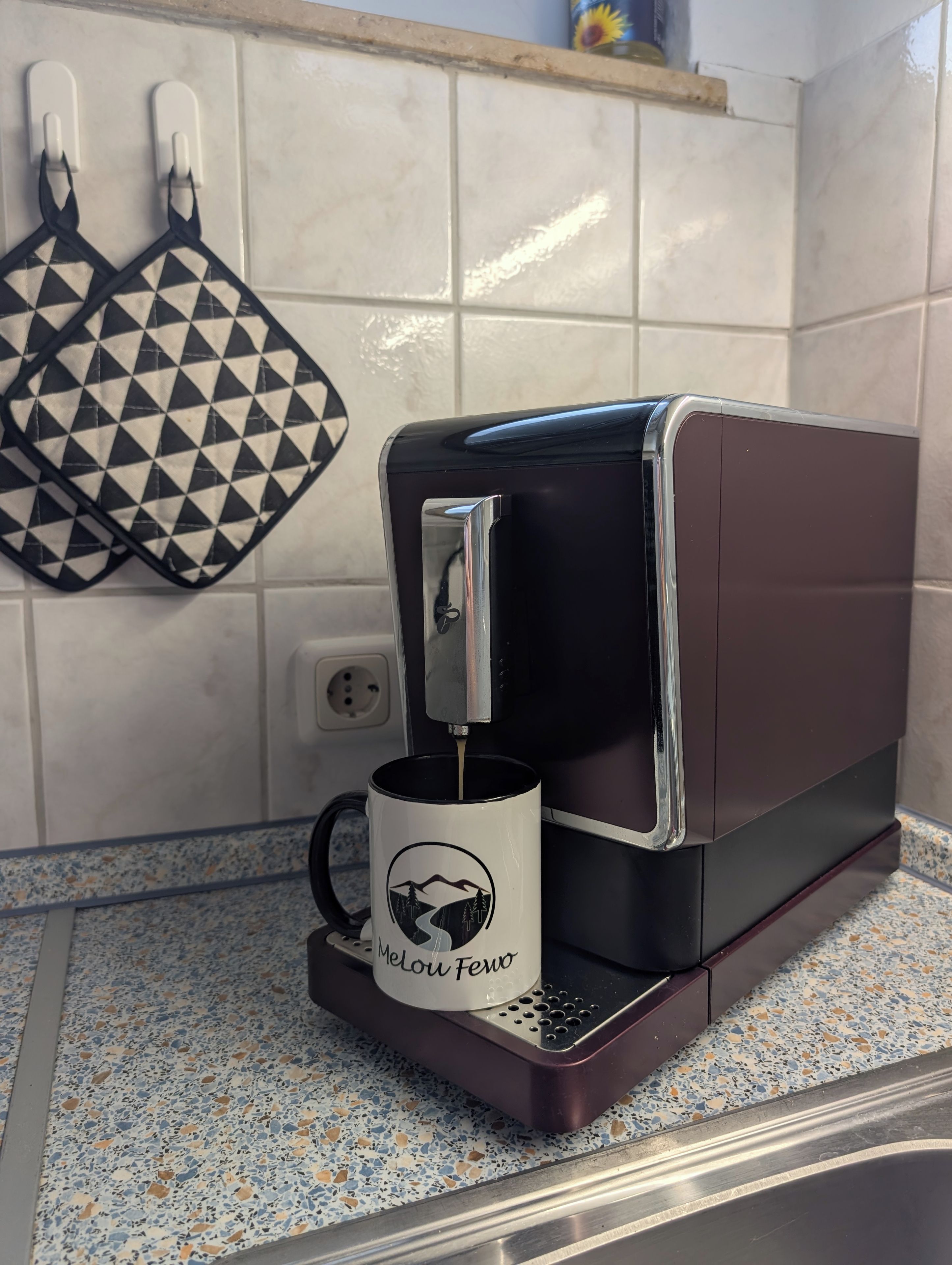 Een koffieapparaat met een mok op de lekbak, een betegelde spatwand en een aanrecht met een streeppatroon.