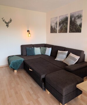 Ein modernes Wohnzimmer mit Ecksofa, einem kleinen Tisch und einer Wanddekoration.