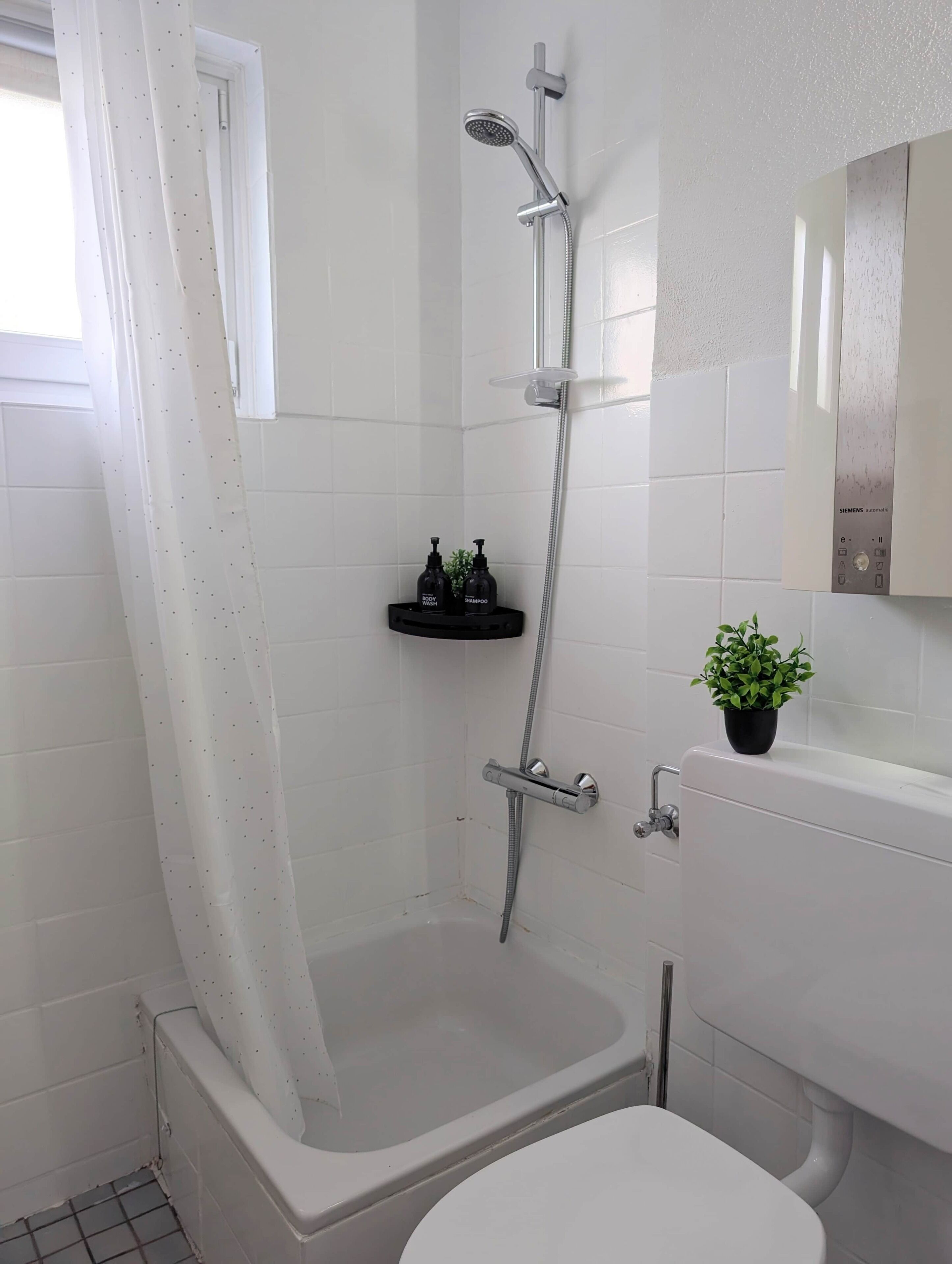 Ein Badezimmer mit Dusche, Toilette und einer kleinen Ablage für Pflegeprodukte.