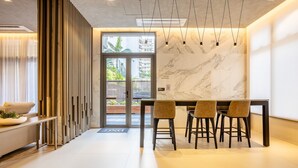 A modern interior with a marble wall, a dining area with chairs, and a view through a glass door. - Your Perfect and Exclusive Stay in the Heart of Itaim Bibi - DSG (São Paulo)