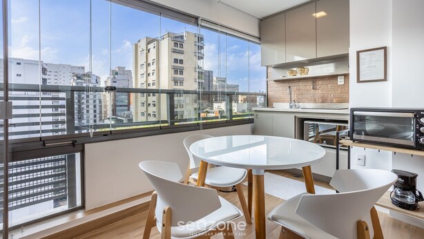 A modern kitchen with a round dining table and white chairs, large windows with a city view, and a built-in oven. - Your Perfect and Exclusive Stay in the Heart of Itaim Bibi - DSG (São Paulo)