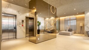 A modern lobby with marble walls, an elevator, a seating area, and a large decorative sculpture. - Your Perfect and Exclusive Stay in the Heart of Itaim Bibi - DSG (São Paulo)