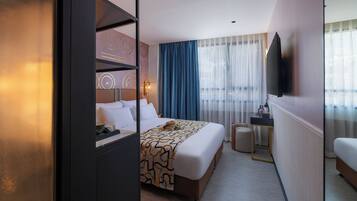 A hotel room with a bed, a desk, a chair, a TV, and a window with curtains.