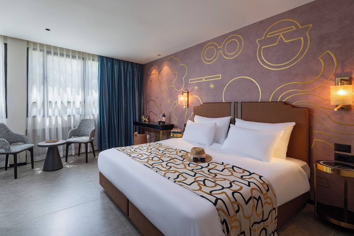Una habitación de hotel con una cama grande, un escritorio, dos sillas y un televisor.