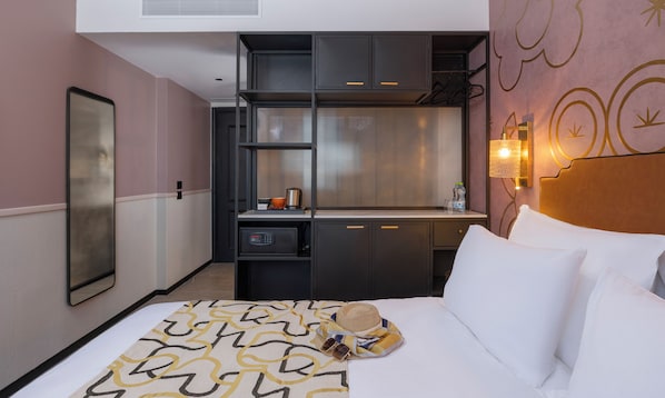 A hotel room with a bed, a small kitchenette, a mirror, and a wall-mounted light fixture. - Iconic Hotel - by Echo Hotels (Tel Aviv)