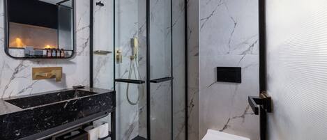 Un baño moderno con ducha de vidrio, lavamanos de mármol negro y un inodoro blanco.