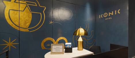 A reception desk with a framed welcome sign, a gold lamp, and a wall with golden geometric designs and the hotel name 'ICONIC HOTEL'.