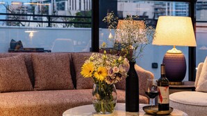 Ein modernes Interieur mit einer Couch, einem runden Tisch mit Blumenvase, einer Lampe und einer Weinflasche.